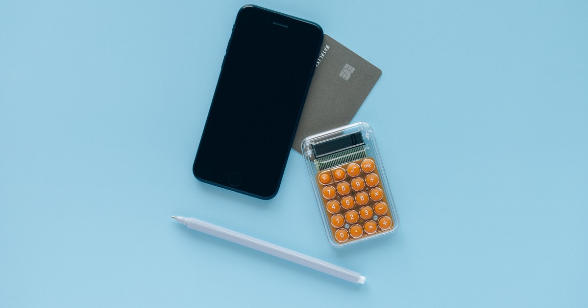 A smartphone, calculator, pen, and credit card atop a blue surface